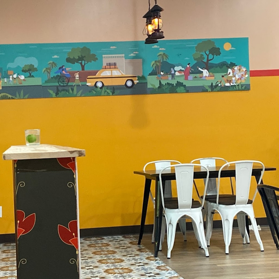 A vibrant Indian-themed mural above a table with white chairs and a decorative stand at Bittoo's Tikka.