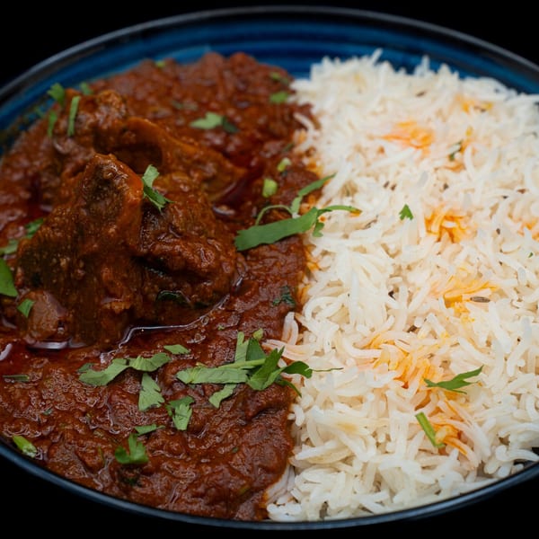 Bittoo's Tikka's Indian curry with meat and cilantro, served with white rice in a blue bowl.