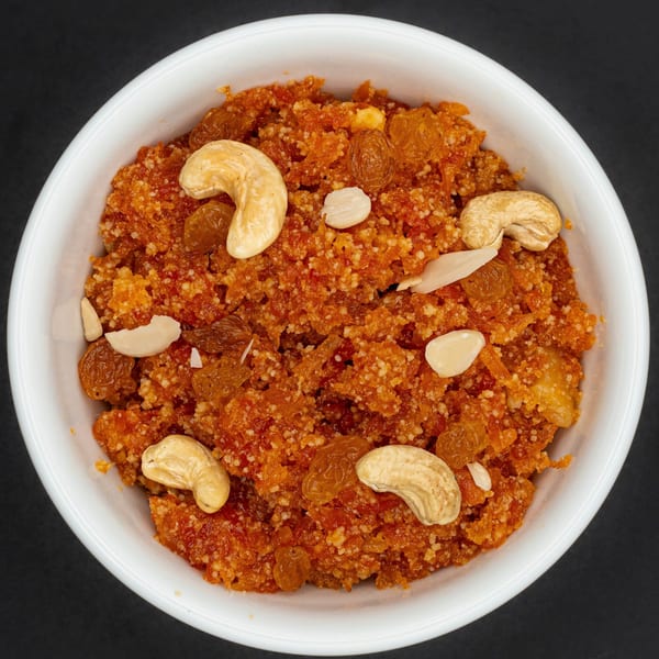 A white bowl filled with orange gajar halwa, garnished with cashews, almonds, and raisins.
