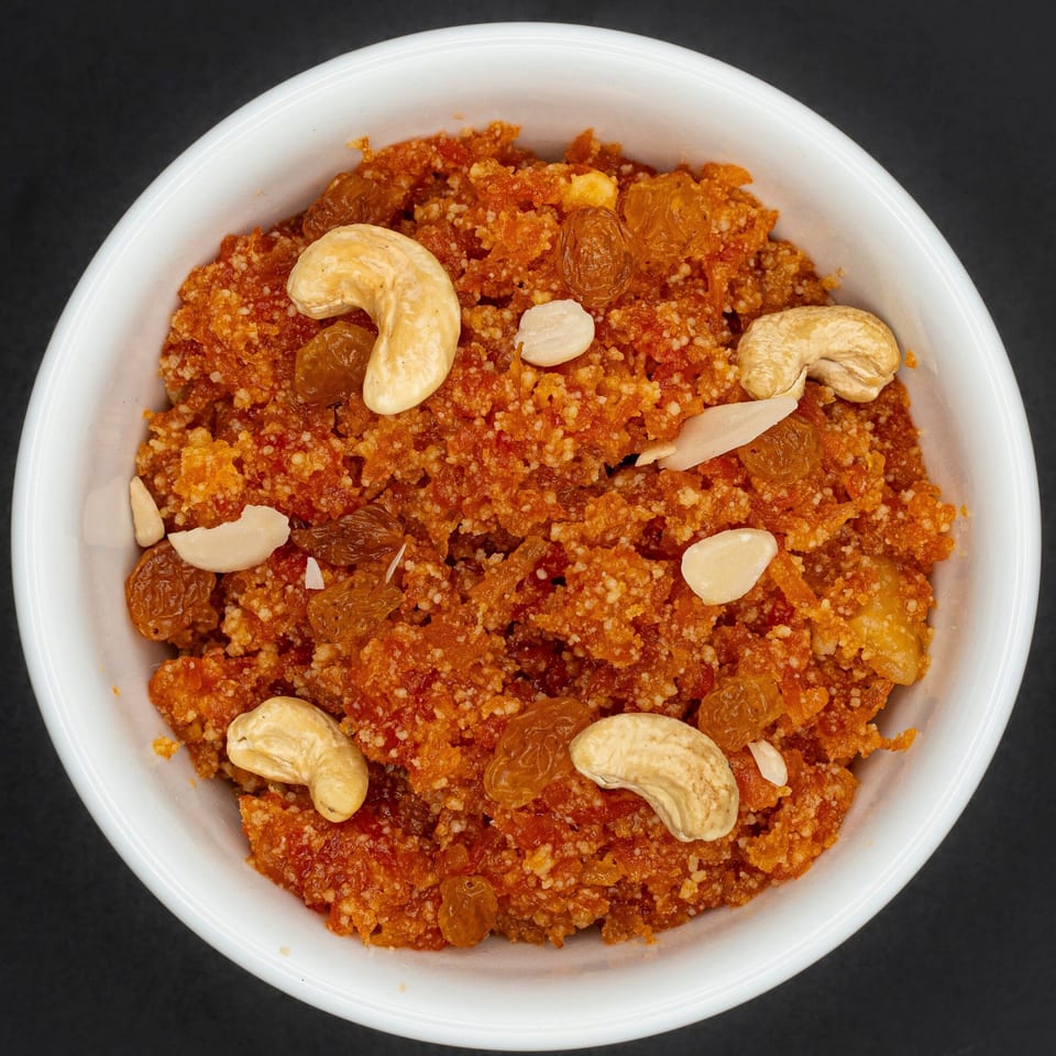 A white bowl filled with orange gajar halwa, garnished with cashews, almonds, and raisins.