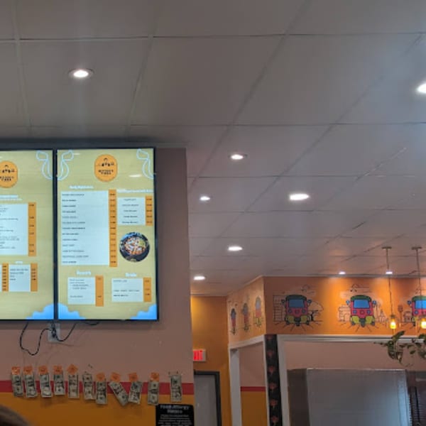 Digital menu boards display Indian food options above a wall decorated with auto-rickshaw murals.