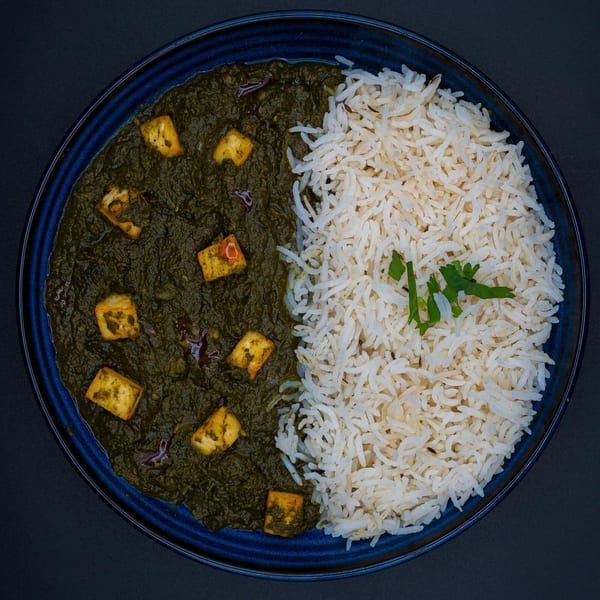 Overhead view of Bittoo's Tikka's Palak Paneer with white rice and a sprig of cilantro.