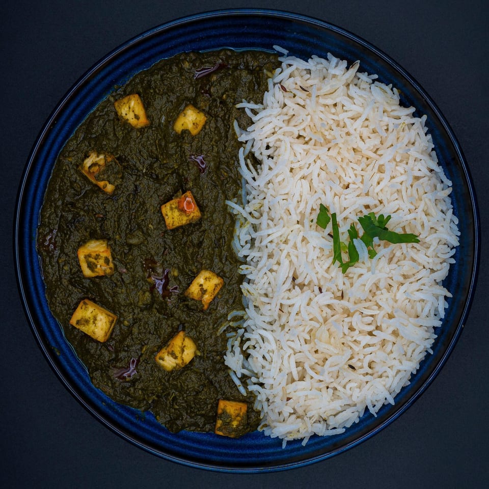 Overhead view of Bittoo's Tikka's Palak Paneer with white rice and a sprig of cilantro.