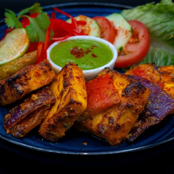 Bittoo's Tikka paneer tikka with green chutney, lime, cilantro, and salad on a blue plate.