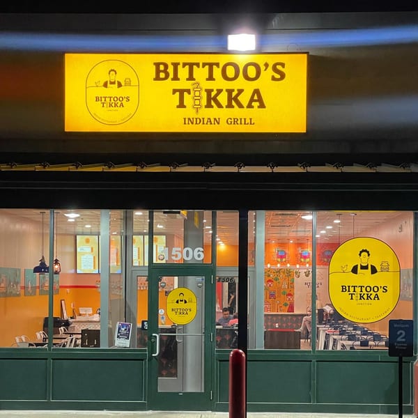 Exterior of Bittoo's Tikka Indian Grill at night, with a bright yellow sign and illuminated interior.